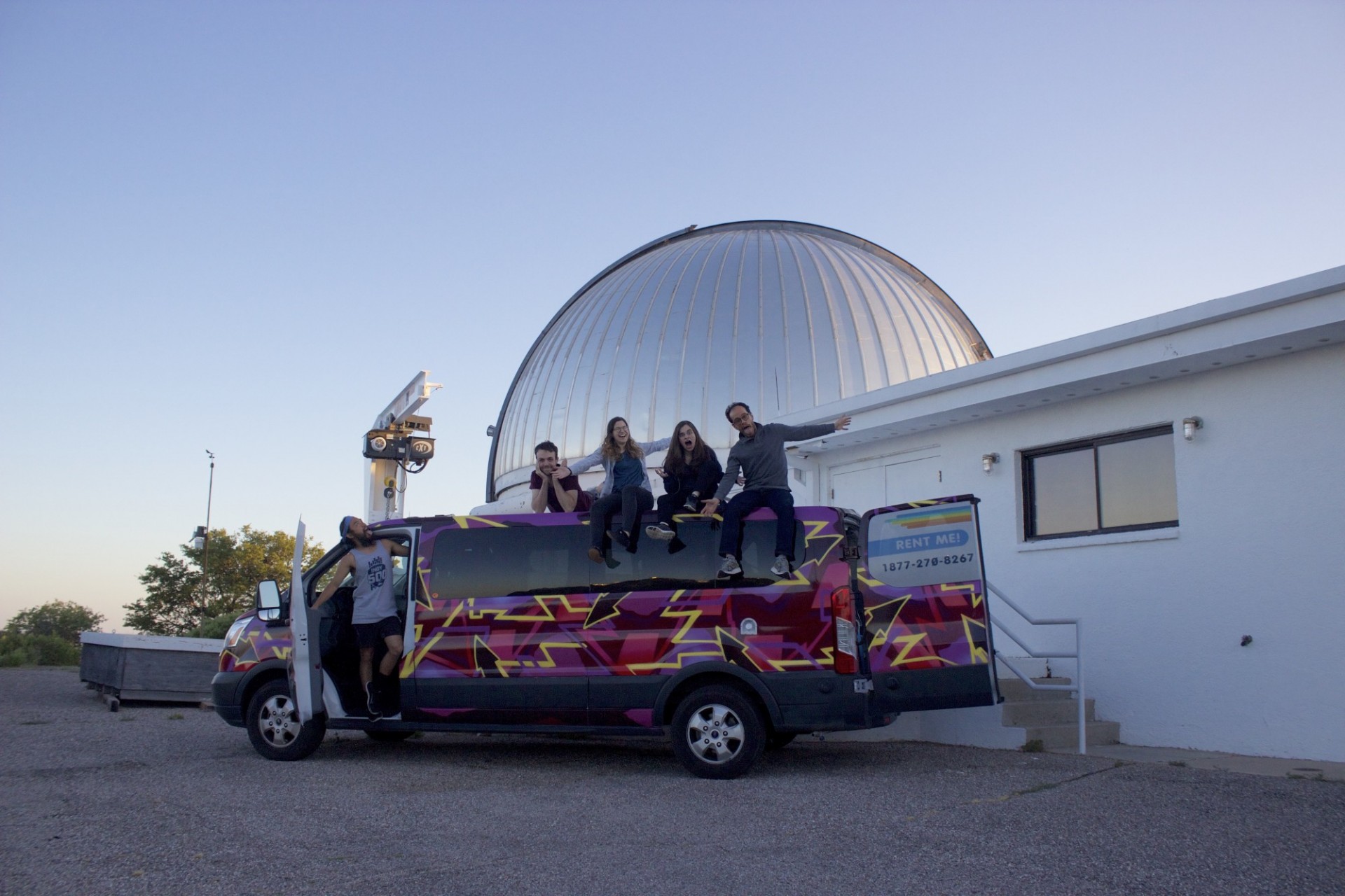 Group members on top of a multicolored van in front of the MDM 2.4 m telescope.